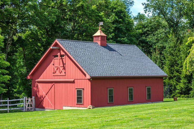 A red barn with a blue roof is sitting in the middle of a grassy field.