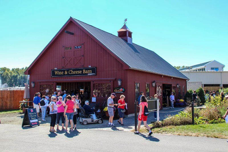 A group of people are standing outside of a red barn that says wine & cheese barn