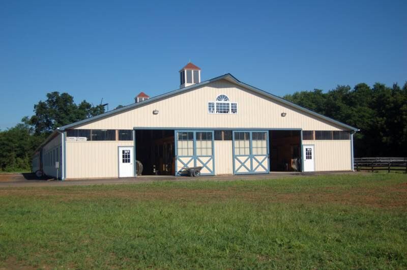 A large white barn with blue doors is sitting in the middle of a grassy field.