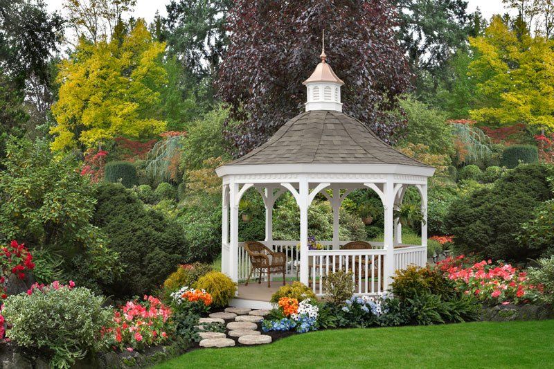 A white gazebo is surrounded by flowers and trees in a garden