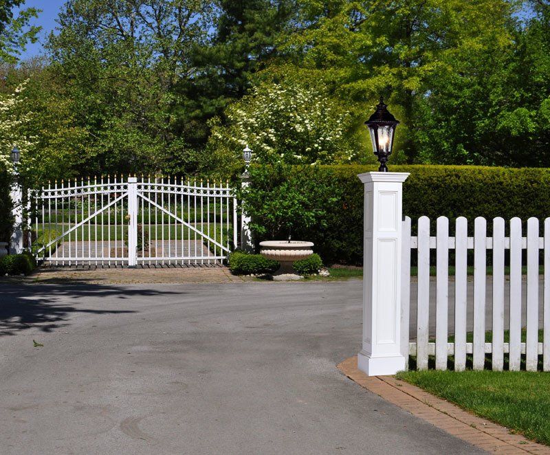A white picket fence surrounds a driveway with a gate