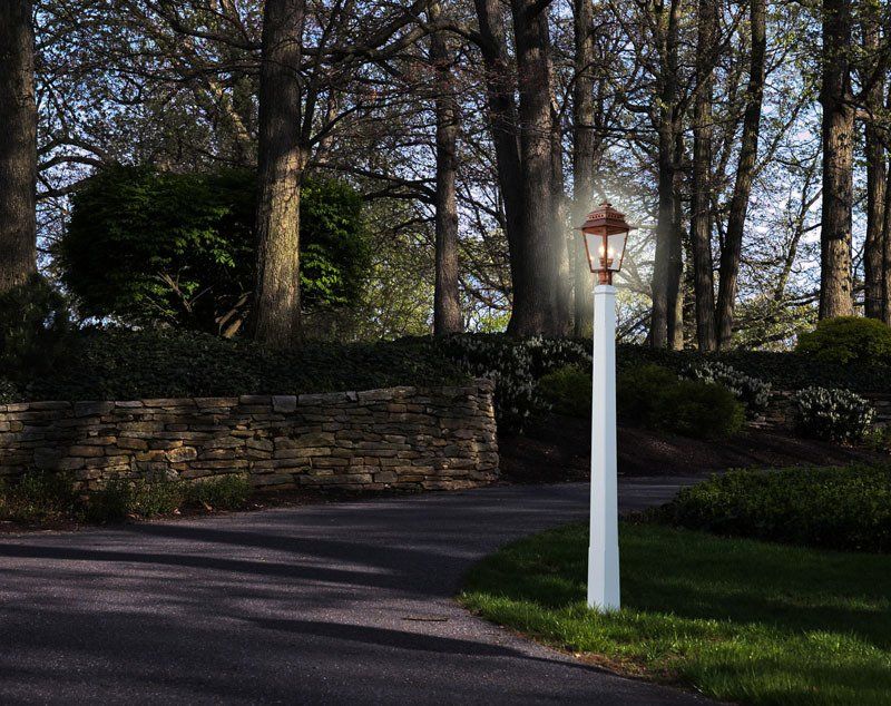 A lamp post in the middle of a driveway with trees in the background