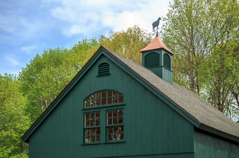 A green barn with a weather vane on top of it