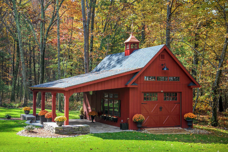 A red barn with a porch in the middle of a lush green field.