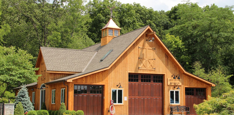 a large wooden barn with a cupola on top of it is surrounded by trees .