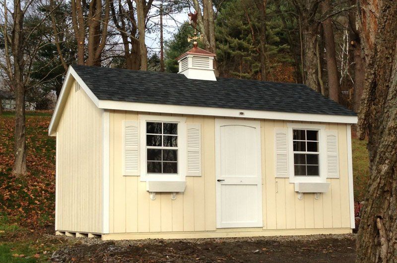 A yellow shed with a black roof and white windows