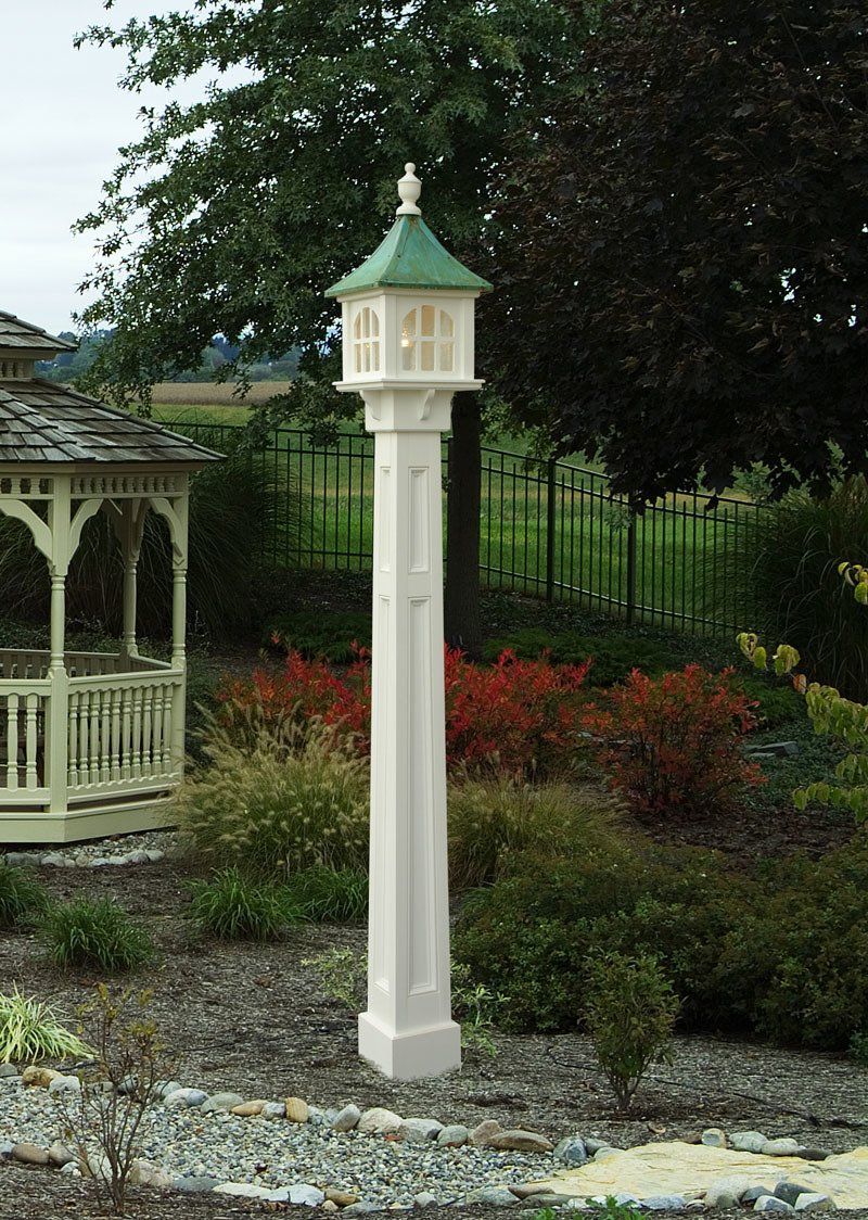 A white pole with a green top is in a garden next to a gazebo.