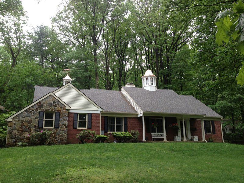 A brick house with a porch in the middle of a lush green forest