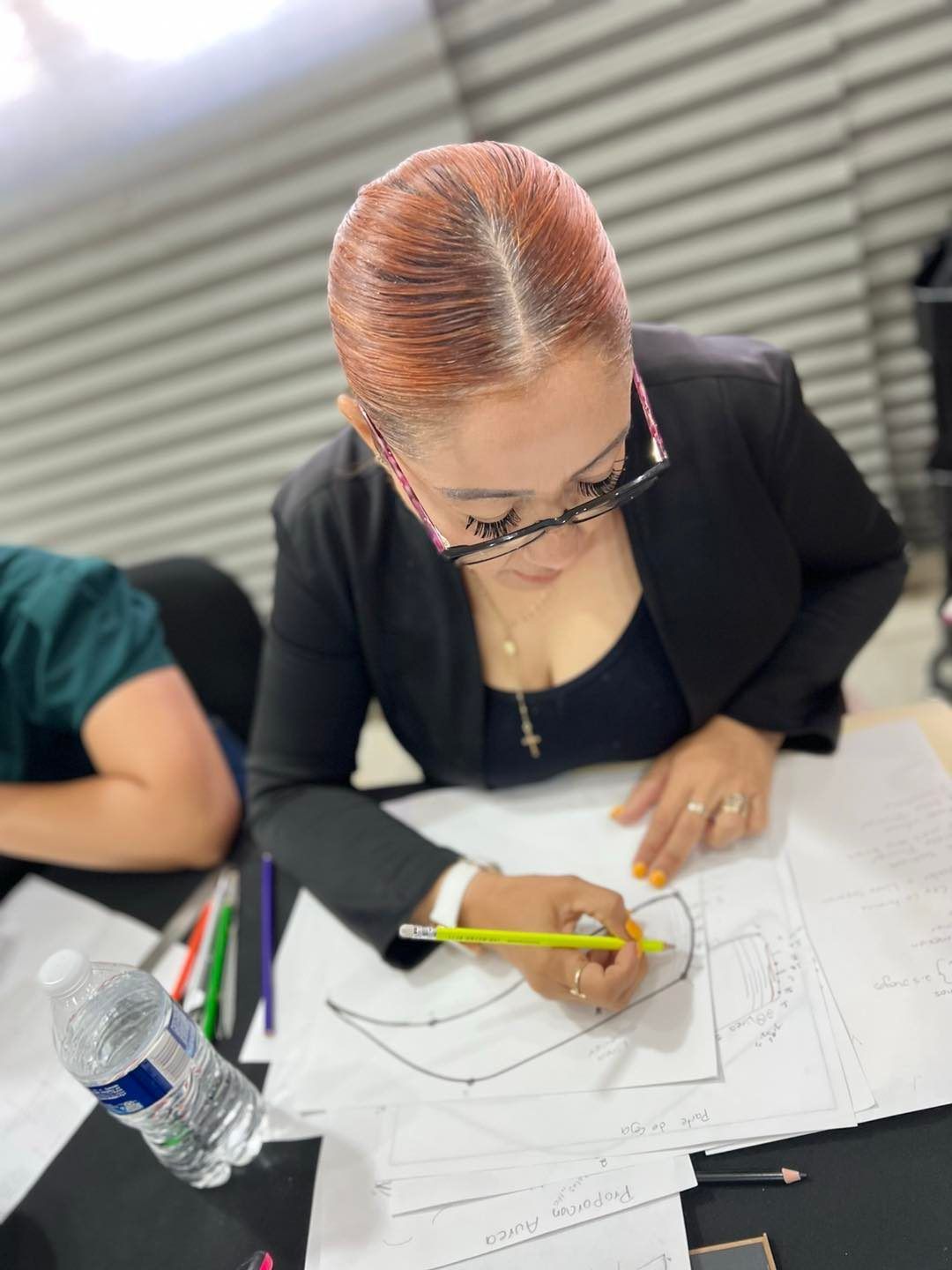 Una mujer está sentada en una mesa dibujando con un lápiz.