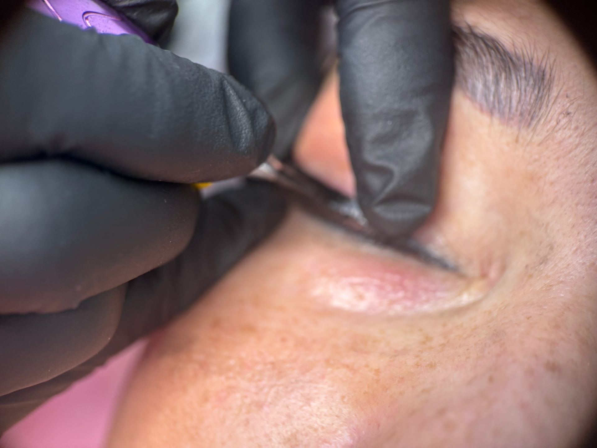 Una persona que lleva guantes negros está aplicando delineador de ojos en el ojo de una mujer.
