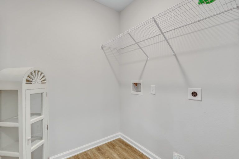 A laundry room with a white cabinet and a wire rack on the wall.