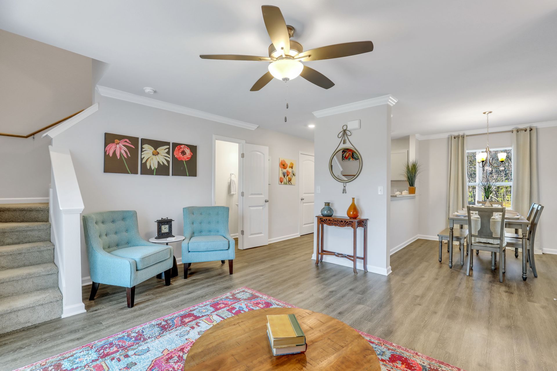 A living room with a ceiling fan , chairs , a table and stairs.