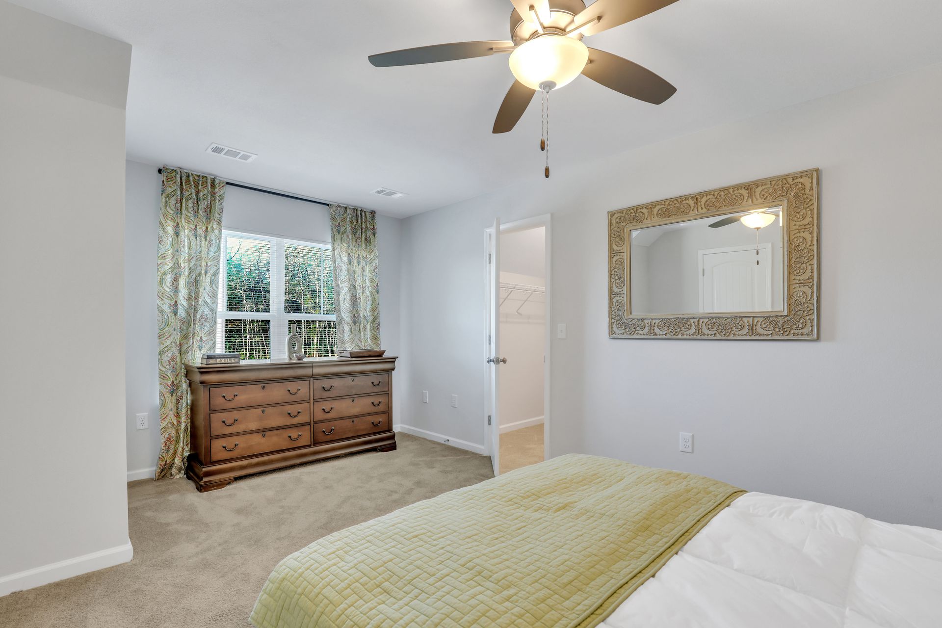 A bedroom with a bed , dresser , mirror and ceiling fan.