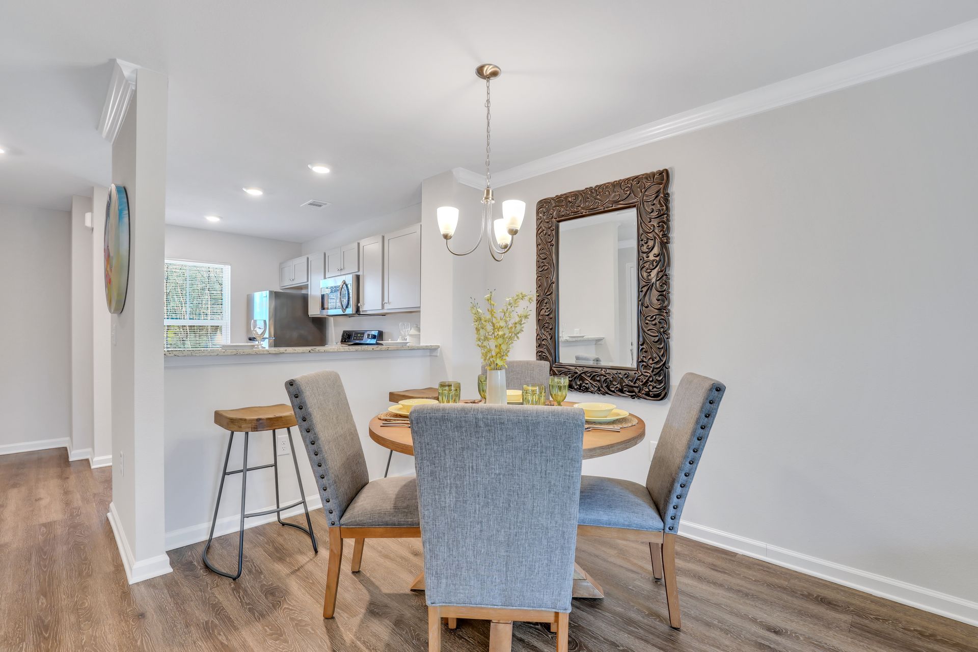 A dining room with a round table and chairs and a mirror on the wall.