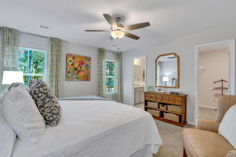 A bedroom with a bed , chair , dresser , mirror and ceiling fan.