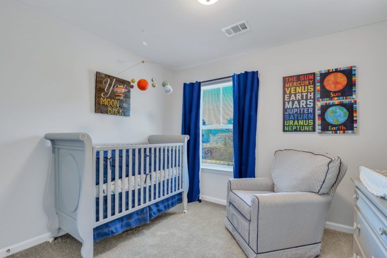 A baby room with a crib , chair , dresser and window.