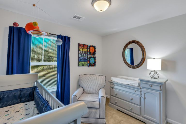 A baby room with a crib , chair , dresser and mirror.