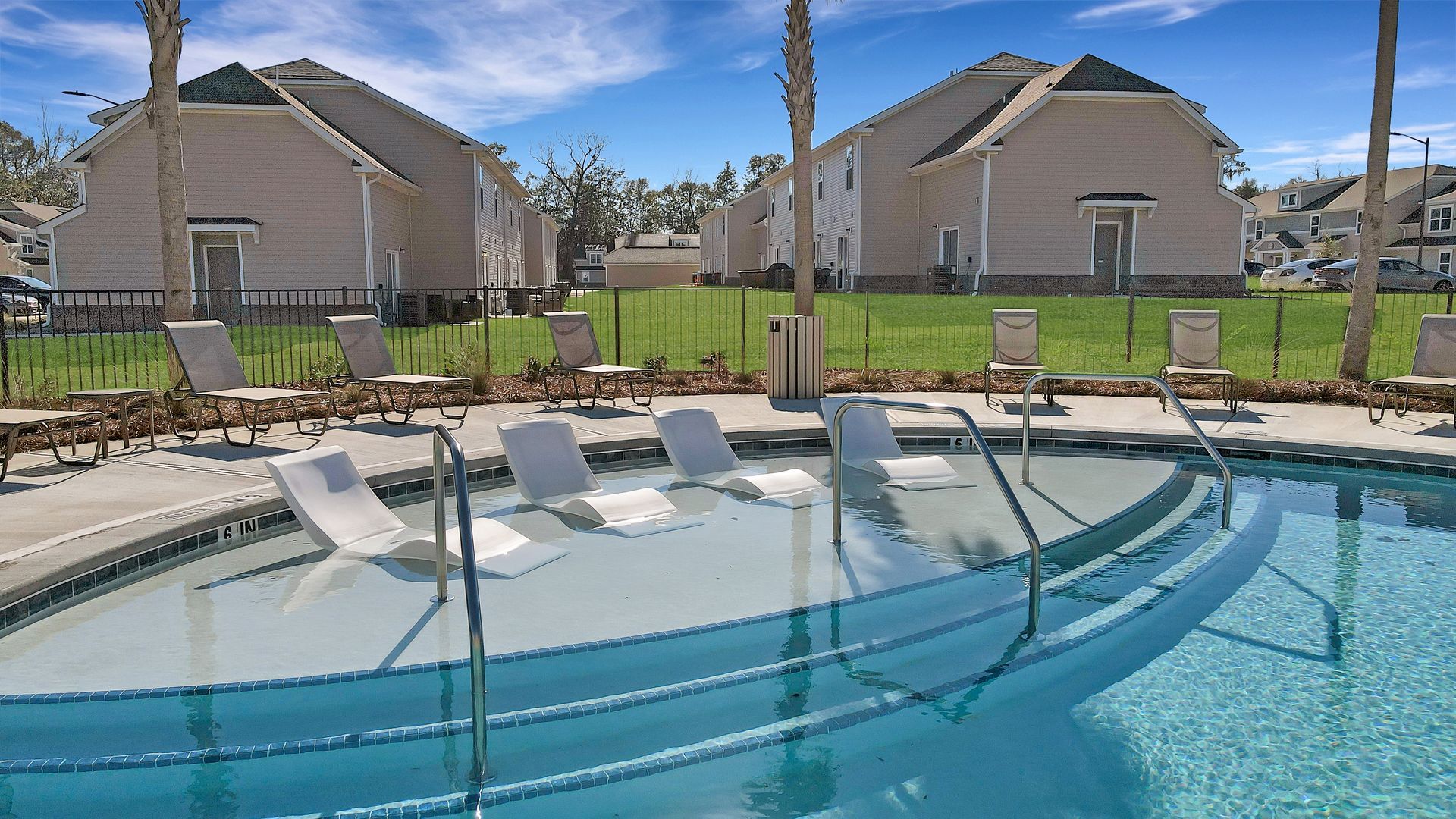 A large swimming pool with chairs around it and houses in the background.