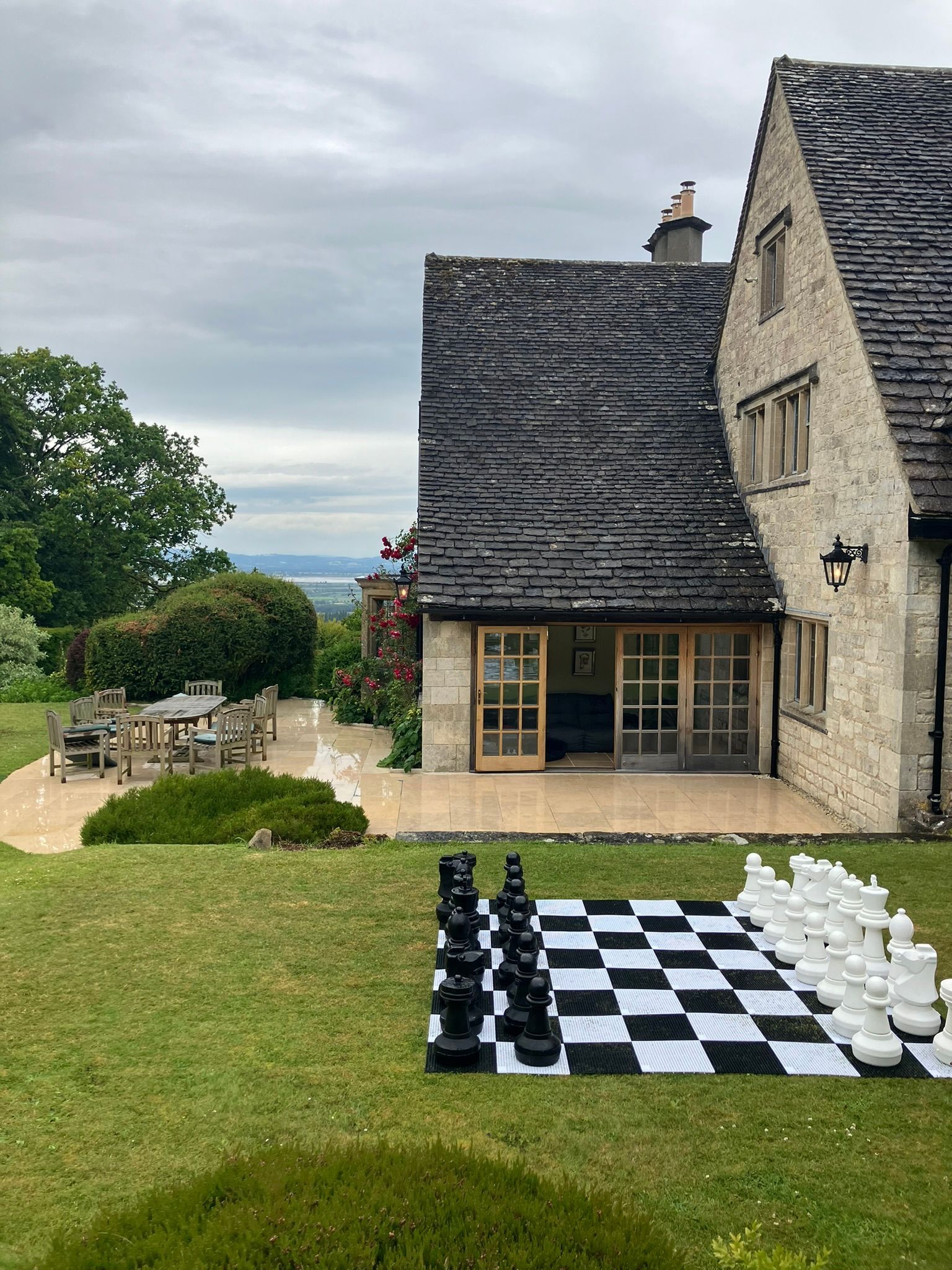 White and black chess board on a garden of grass.  With giant chess pieces.  A large brick home in the back ground.