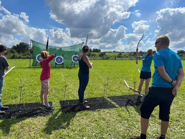 3 archery targets with safety net.  4 people shooting and an instructor watching