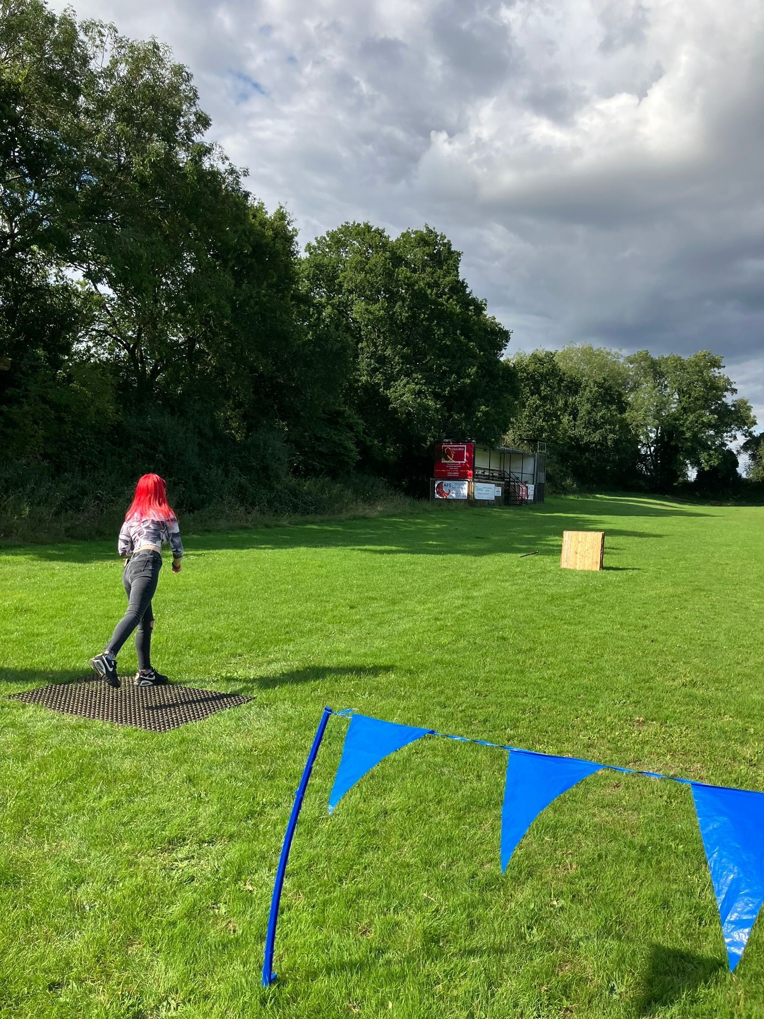 A wooden axe throwing target on a field with a woman throwing an axe towards it