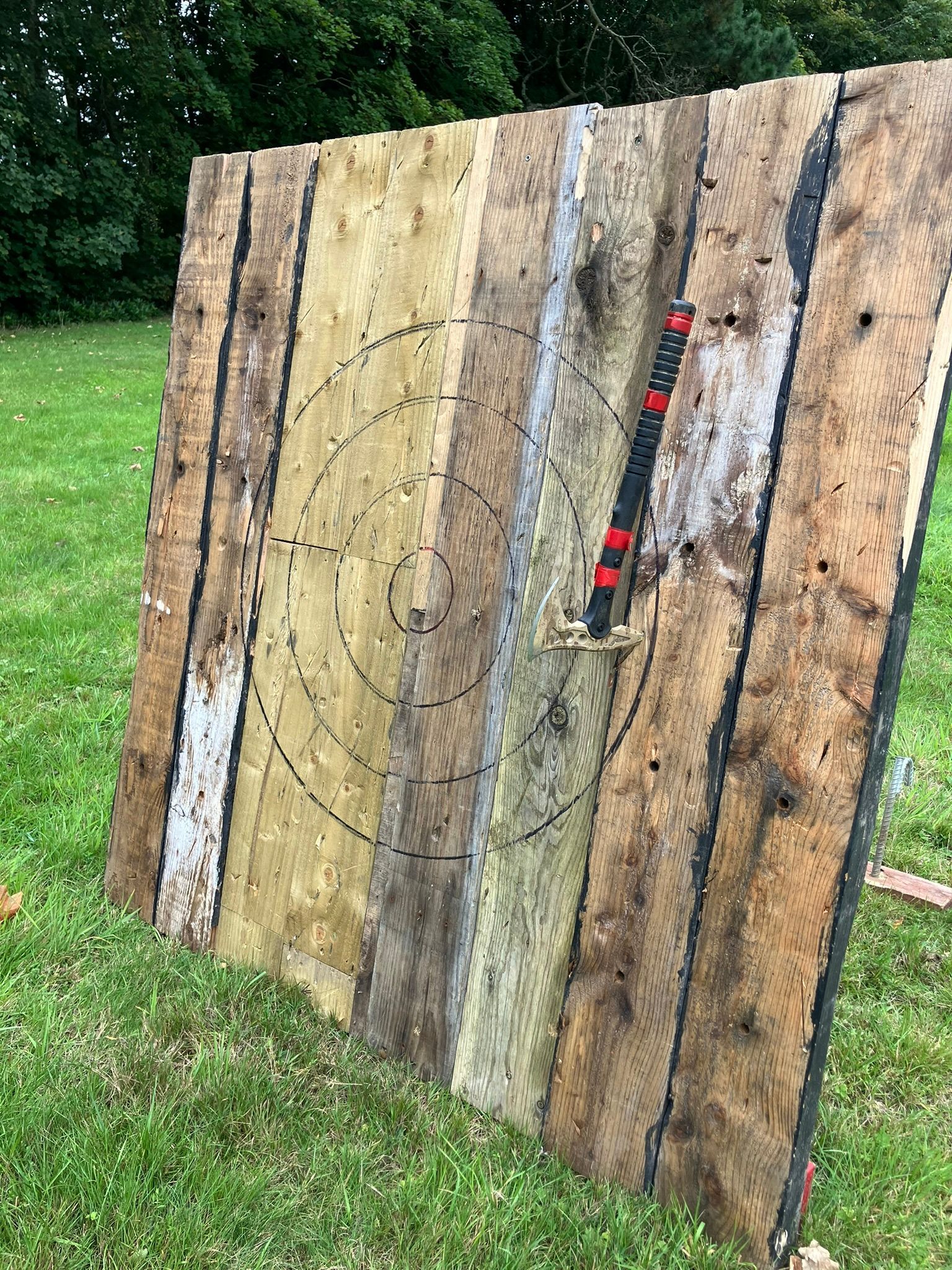 Large wooden axe throwing target with an axe stuck upside down in it