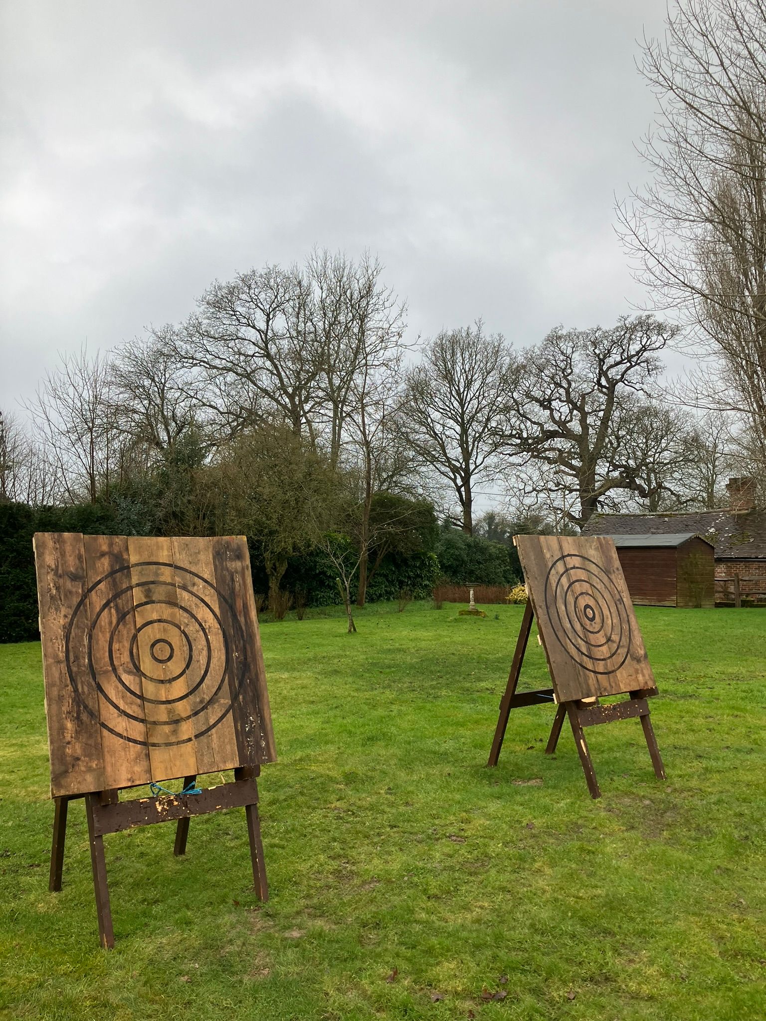 2 wooden axe throwing targets on a field at a holiday home.  Trees in the background.