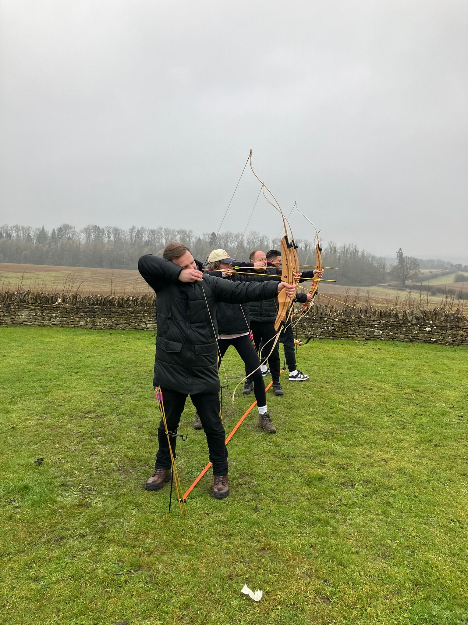 A young woman holding a bow, aimed at an archery target.  There are 2 targets in the photo.