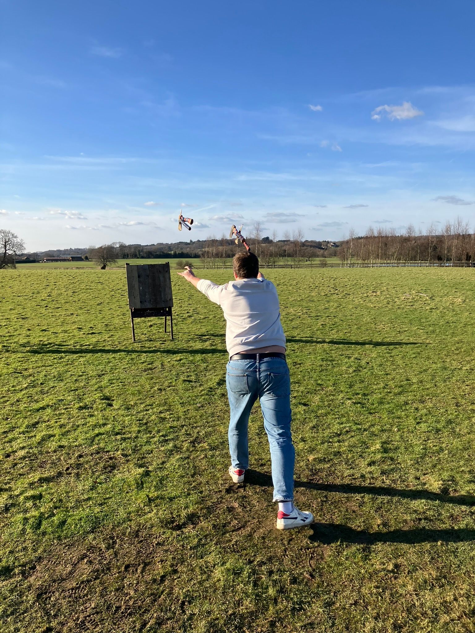 A wooden axe throwing target on a field with a man throwing an axe towards it