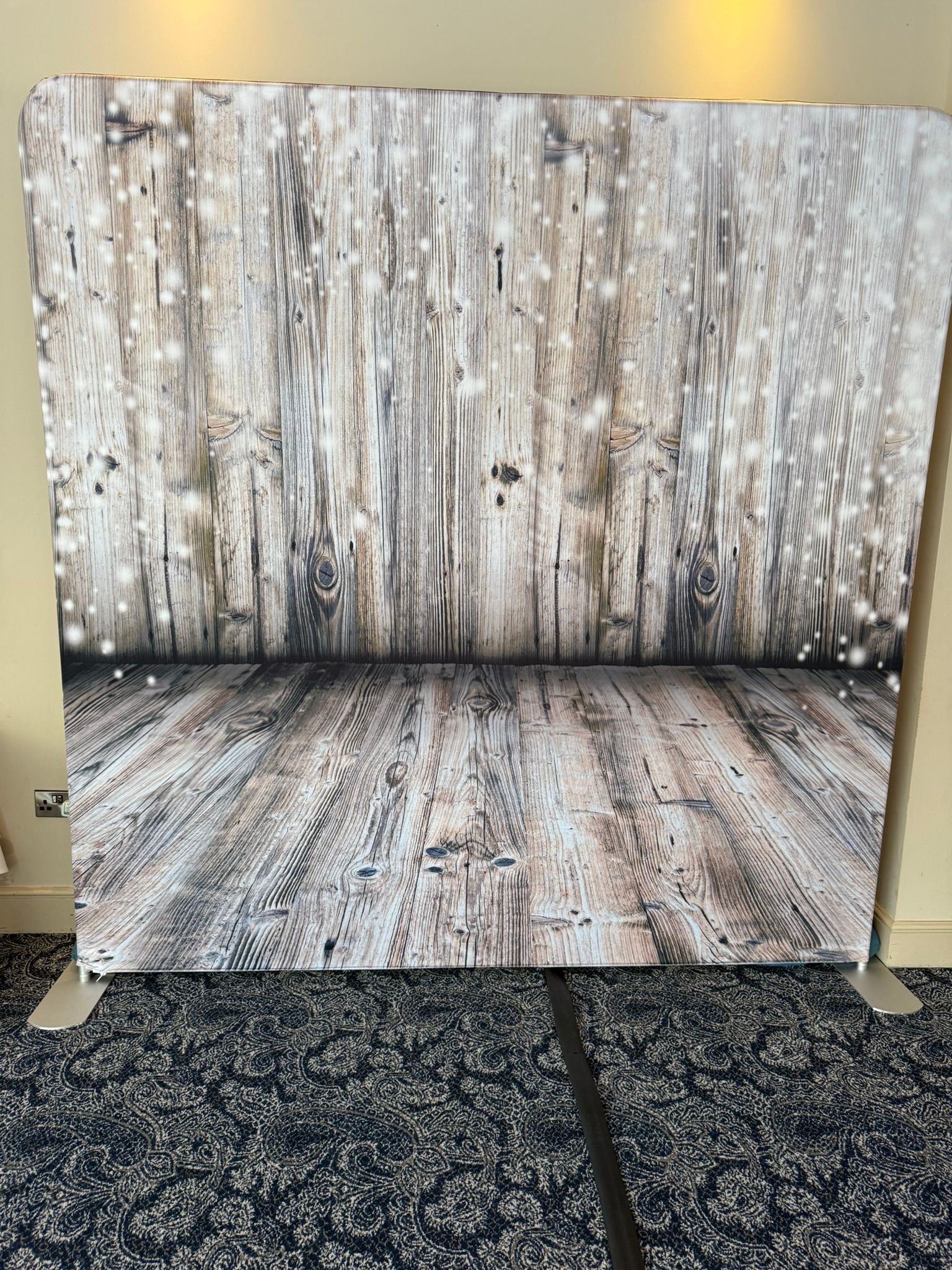8 foot by 8 foot tall square backdrop.  Main colour is a grey wooden design with twinkly lights.  In front of a grey curtain.