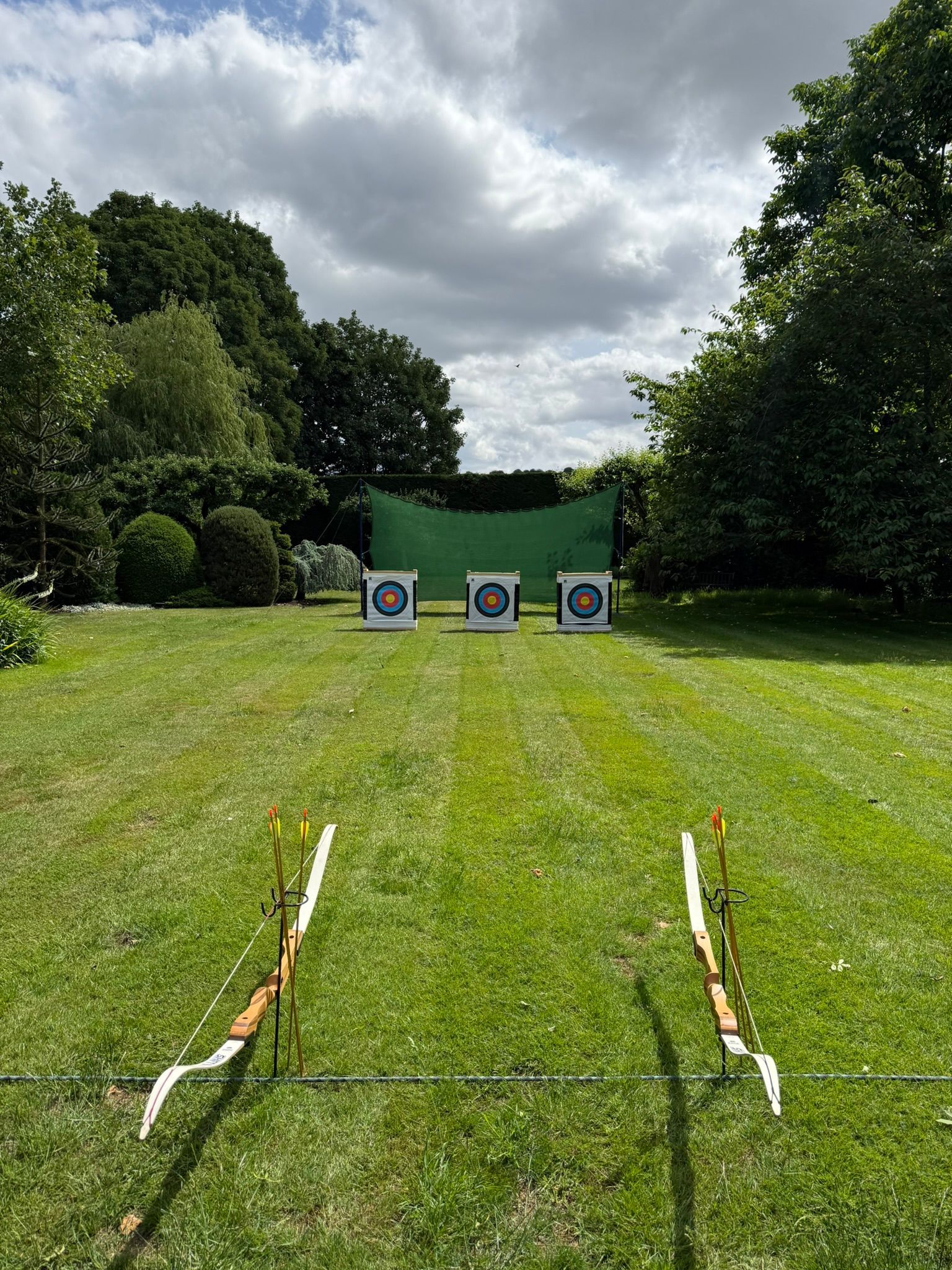 Archery bows and arrows set up in a line on a field with 3 targets in the distance