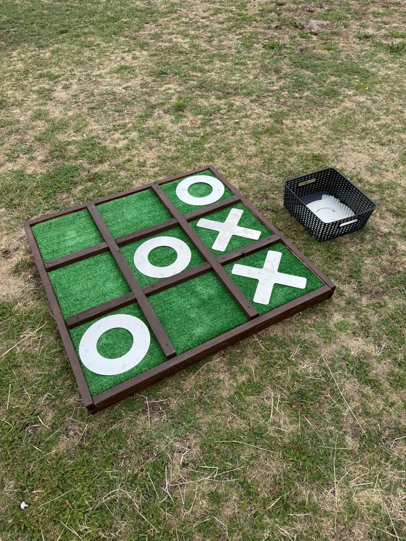 Giant noughts and crosses made out of reclaimed timbers and astro turf, with metal shapes.