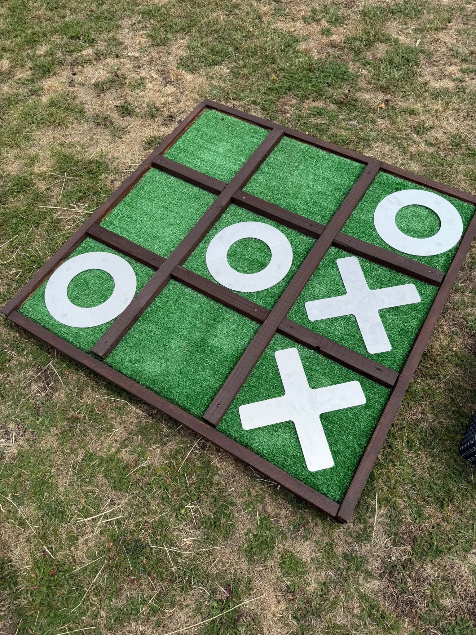 Giant noughts and crosses made out of reclaimed timbers and astro turf, with metal shapes.