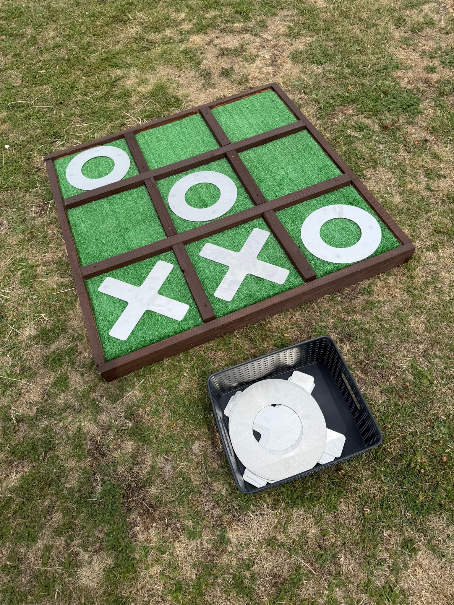 Giant noughts and crosses made out of reclaimed timbers and astro turf, with metal shapes.