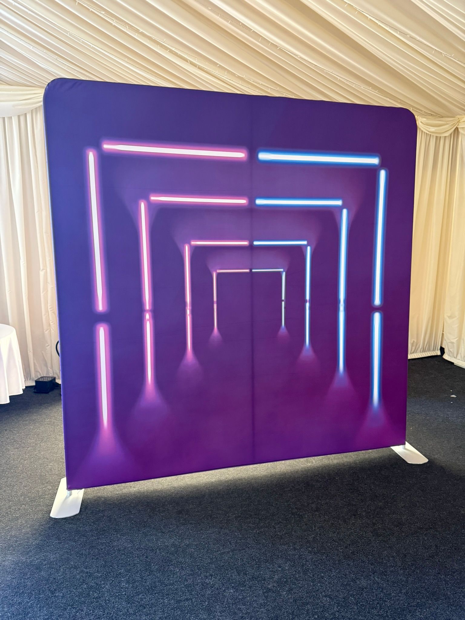 8 foot by 8 foot tall square backdrop.  Main colour is purple with neon arches.  In front of a grey curtain.