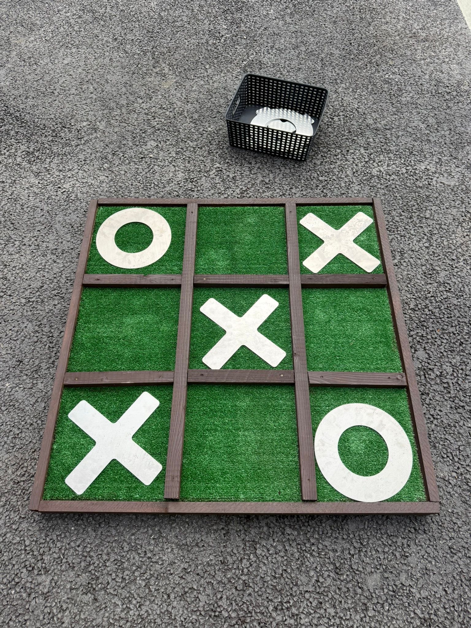 Giant noughts and crosses made out of reclaimed timbers and astro turf, with metal shapes.