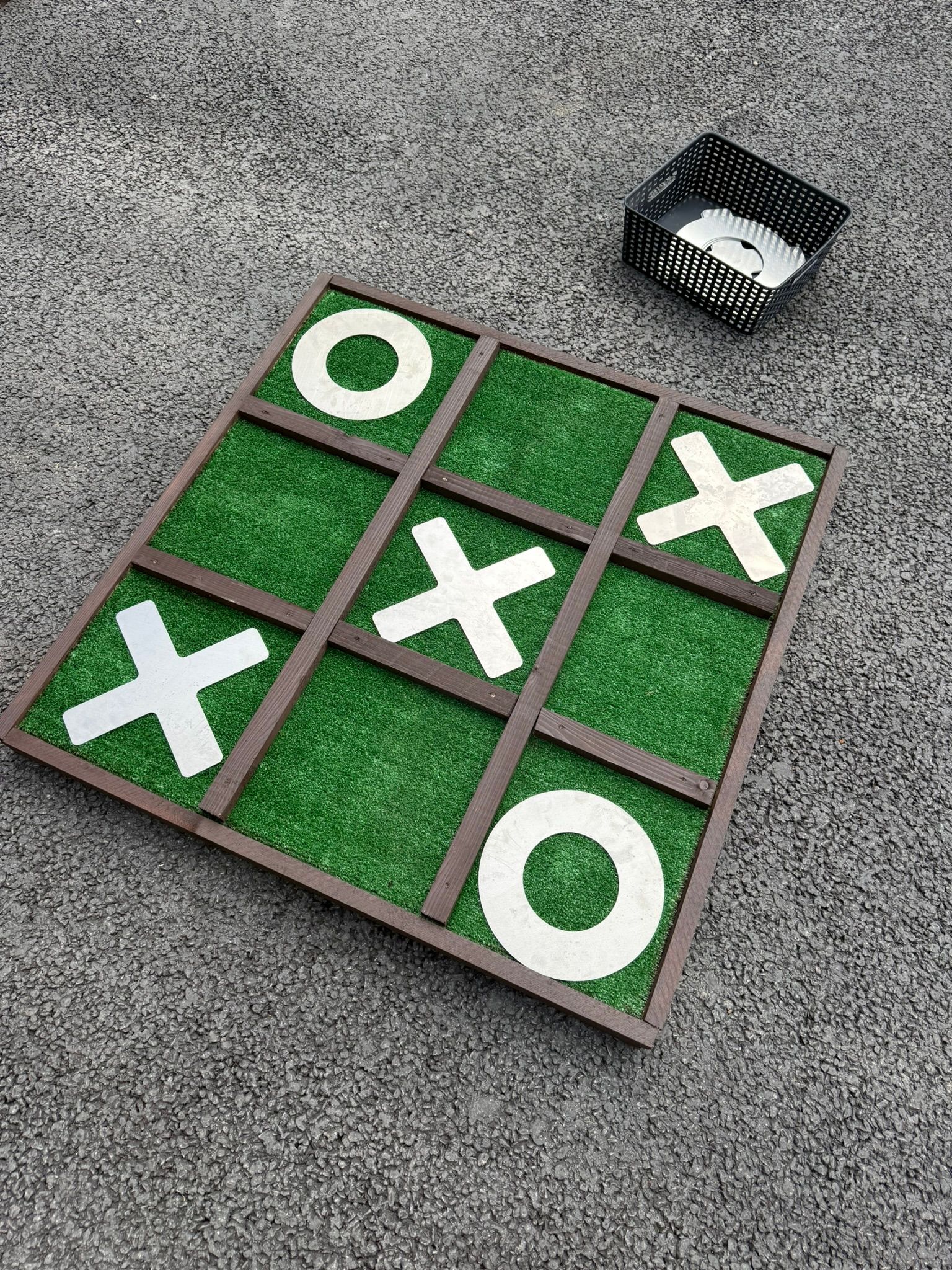 Giant noughts and crosses made out of reclaimed timbers and astro turf, with metal shapes.