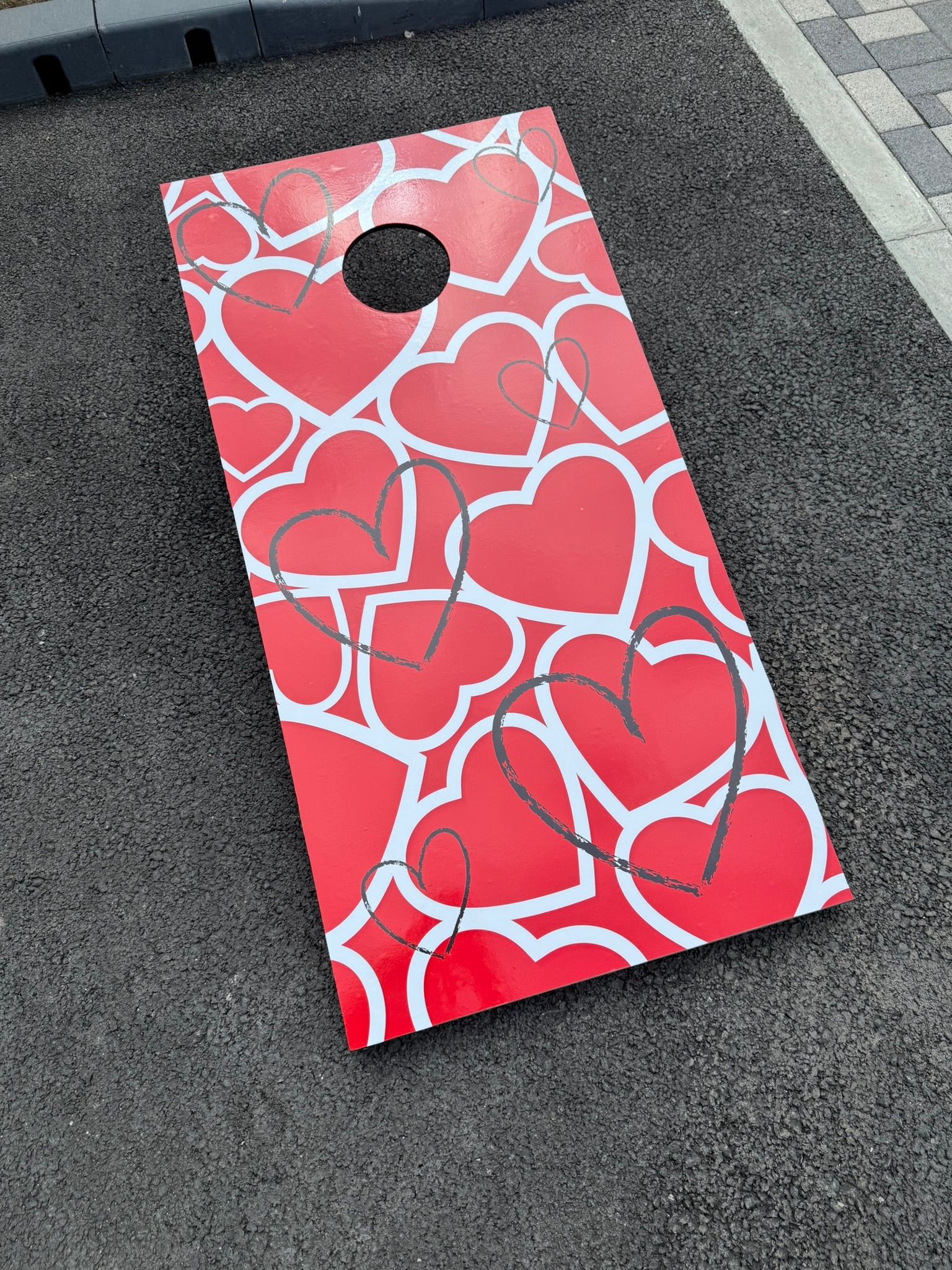 Wooden Cornhole lawn game with 3 bean bags and an information sign on grass at a hotel
