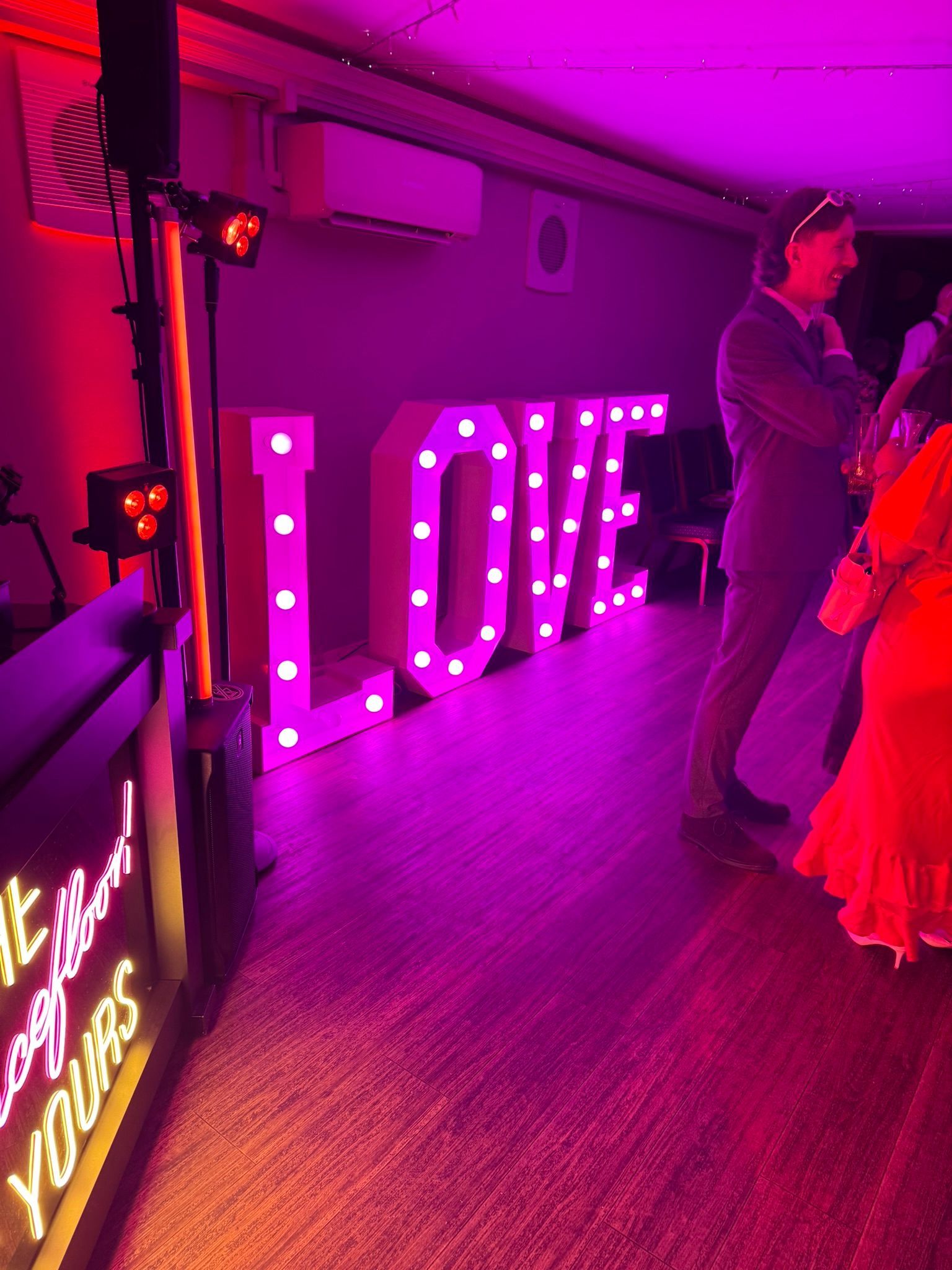 light up letters spelling LOVE, with lights in white colour on a dance floor next to a round table with a wedding cake on it