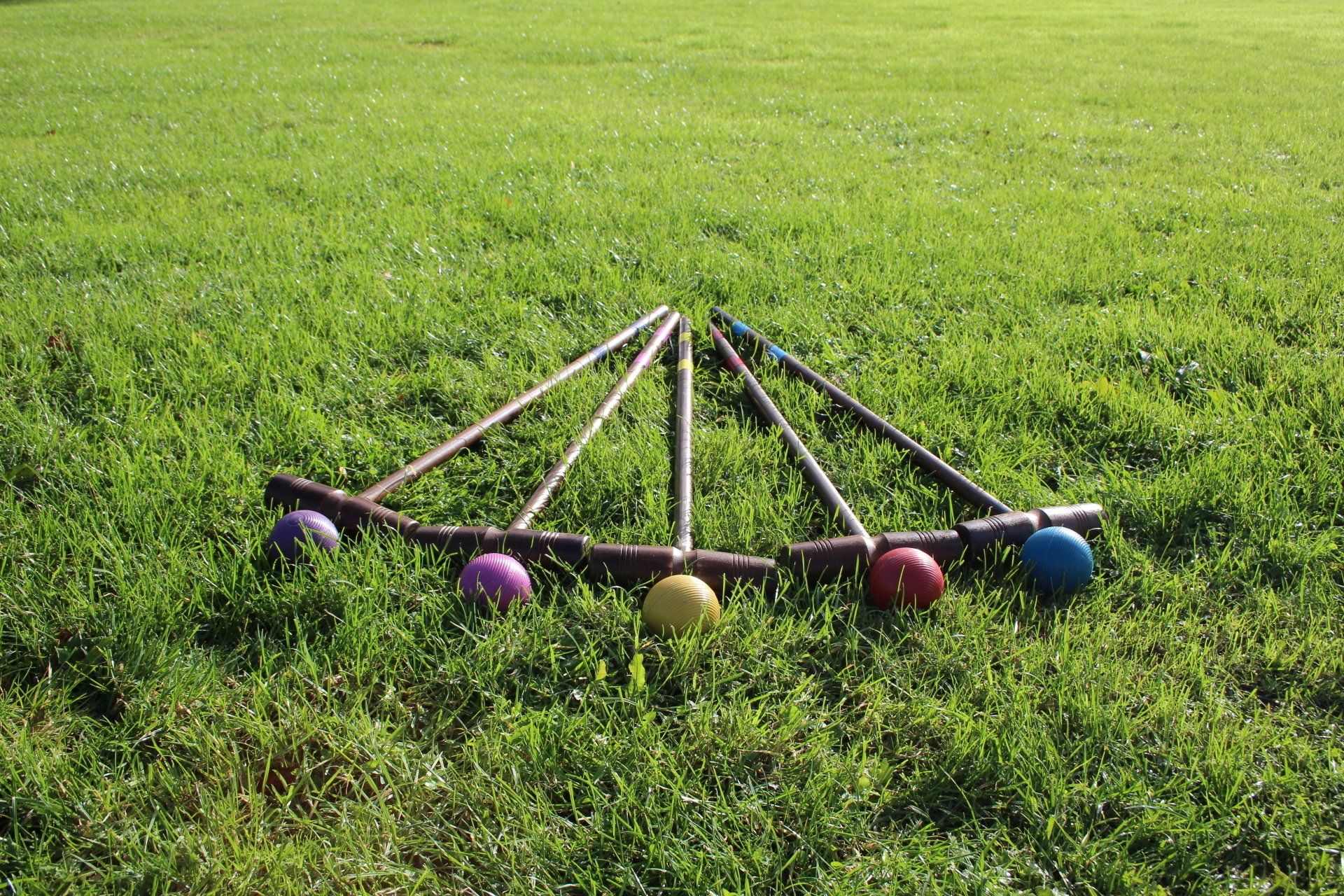 % croquet clubs and 5 balls laid out in a pattern on a green field.