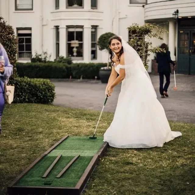 A bride in a white dress playing mini golf
