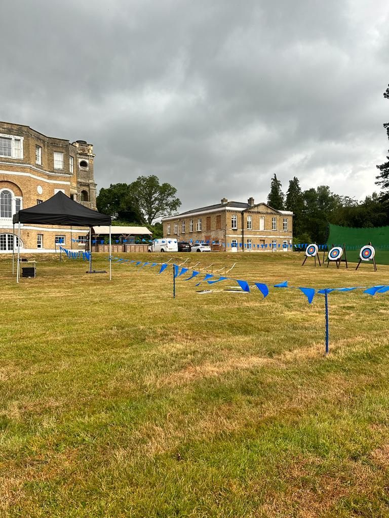 Corporate archery set up on a field at a hotel.  3 targets, pop up gazebo and blue bunting.