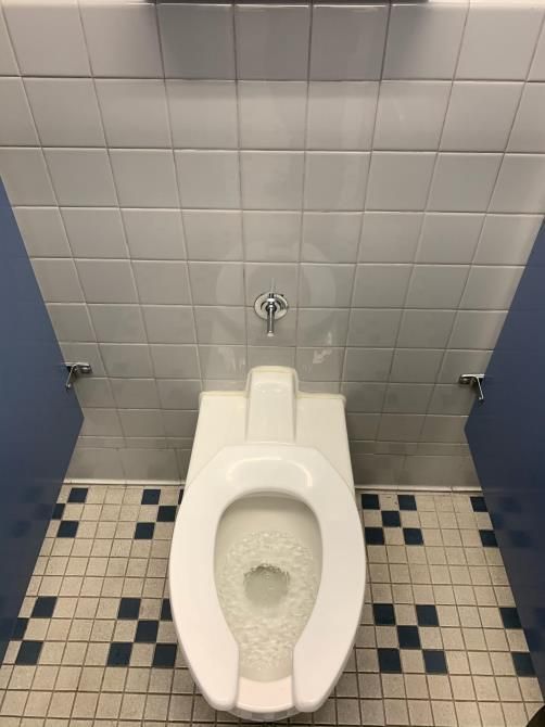 Public restroom with a white toilet, blue-and-white tiled floor, and gray tiled wall.