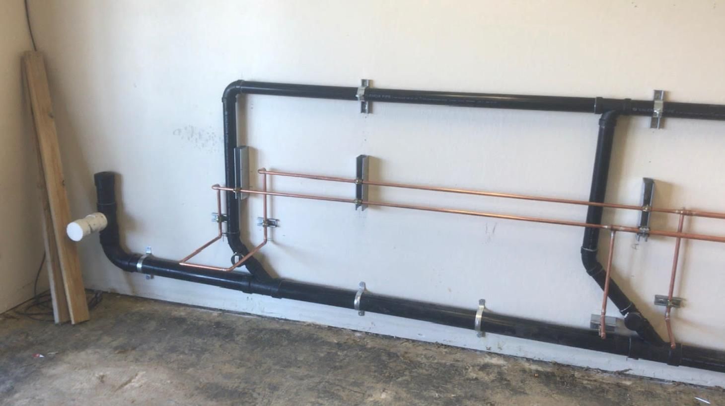 Wall-mounted black and copper pipes installed along a white basement wall.