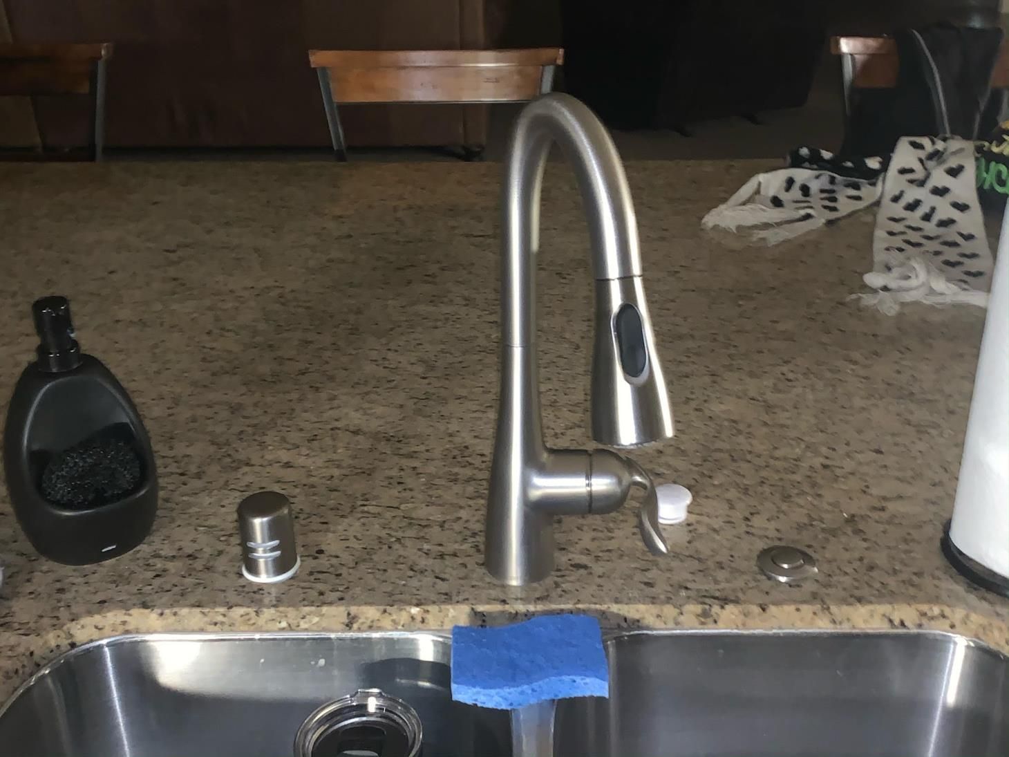 Kitchen sink with stainless faucet, dish soap, a cup, and blue sponge on the counter.