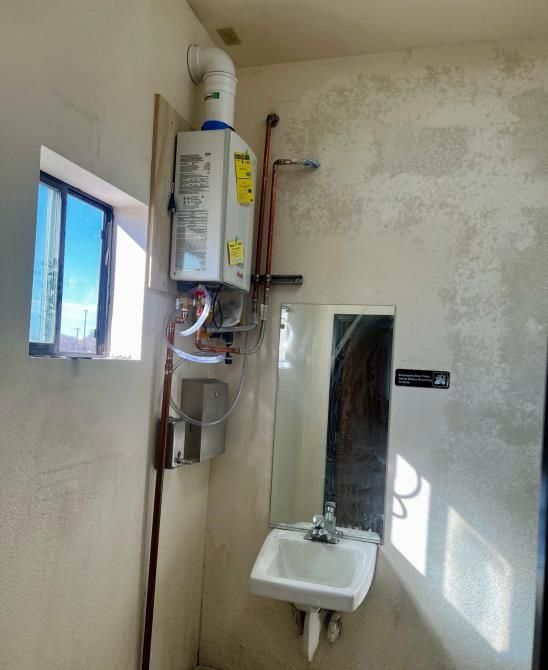 Small bathroom with wall-mounted water heater, mirror, sink, and a window letting in sunlight