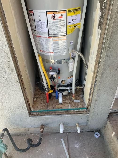 Water heater in a closet with exposed pipes, valves, and wiring around the base.