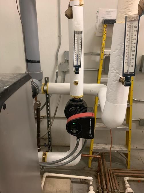 Boiler room piping with valves, gauges, and a red circulation pump in front of white pipes.