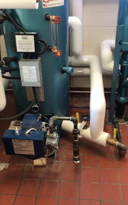 Blue industrial boiler piping and valves with gauges in a mechanical room.
