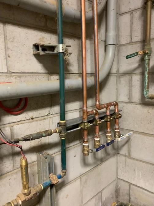 Plumbing pipes and valves against a cinderblock wall in a utility room